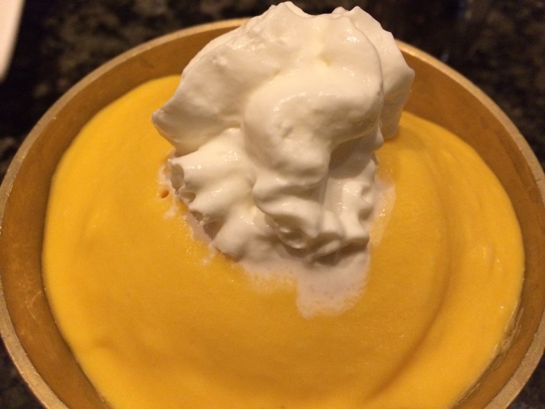 Photo of a bowl of orange-yellow mango ice cream with a dollop of whipped cream on top. 